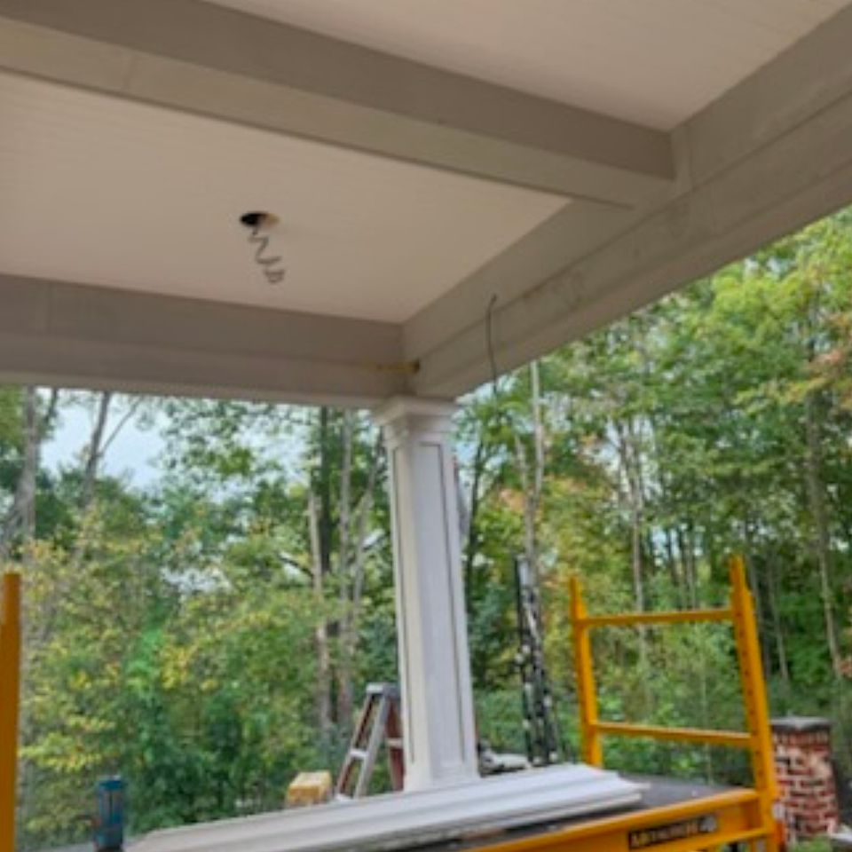 Porch ceiling beams with wired light openings and scaffolding beside a finished square column