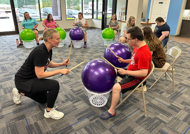 Participants with Down syndrome taking part in a music and movement class using exercise balls as drums with an instructor.