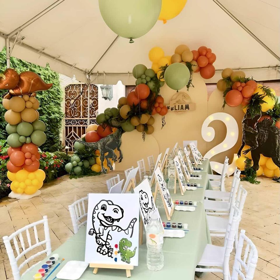 Dinosaur-themed kids’ birthday party with balloon garlands, painting activity table, custom decor, and a giant number 2 backdrop.