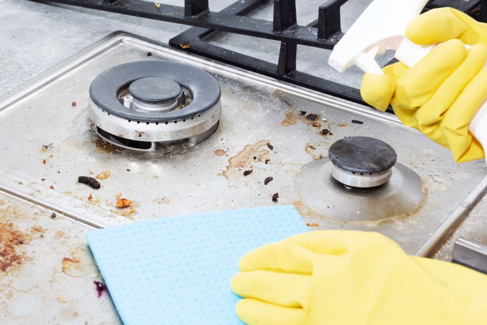 A person with yellow cleaning gloves on cleaning a gas stove