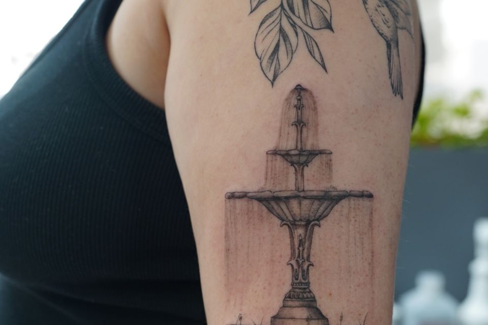 Image of a fountain tattoo in black and grey with detail of water falling down each level of the 3 level fountain