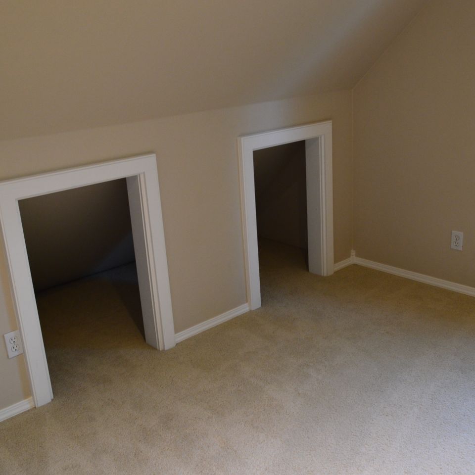 Finished upstairs bonus room with sloped ceiling, twin doorways, and new carpet in a custom home