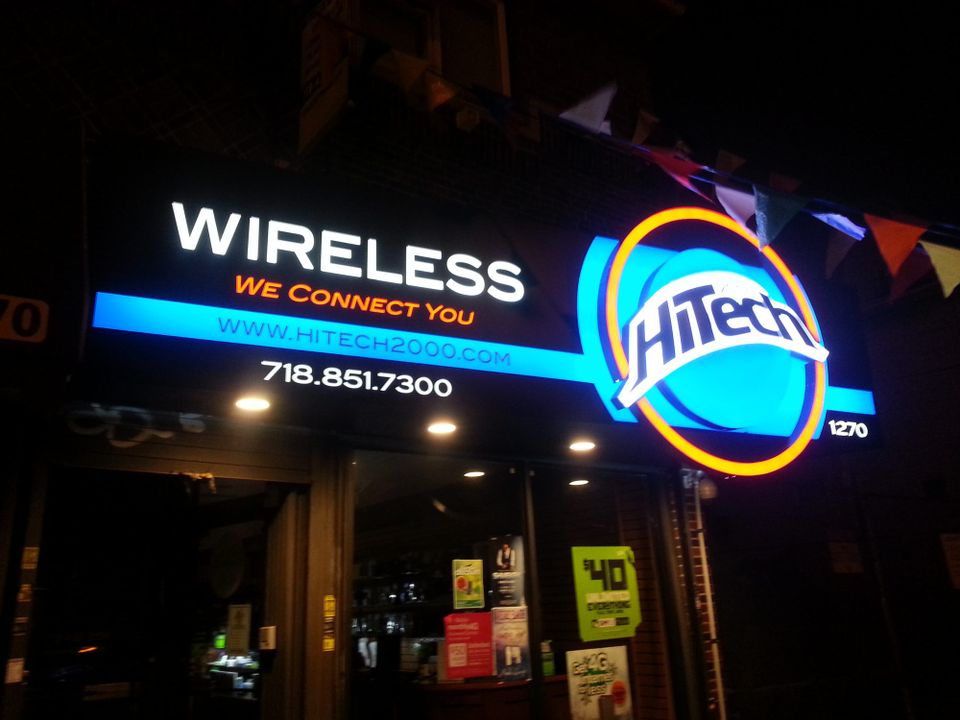 Illuminated HiTech Wireless sign lit at night, with a glowing blue and orange circular logo and white lettering above a storefront