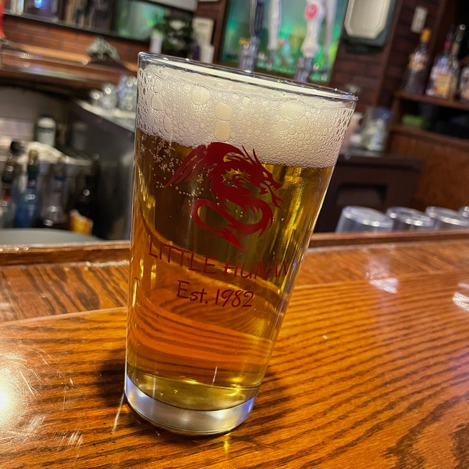 Freshly poured draft beer in a Little Hunan glass sitting on the restaurant bar counter.