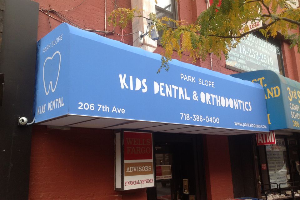 Bright blue custom storefront awning with a printed tooth logo and lettering on a Park Slope dental office in Brooklyn