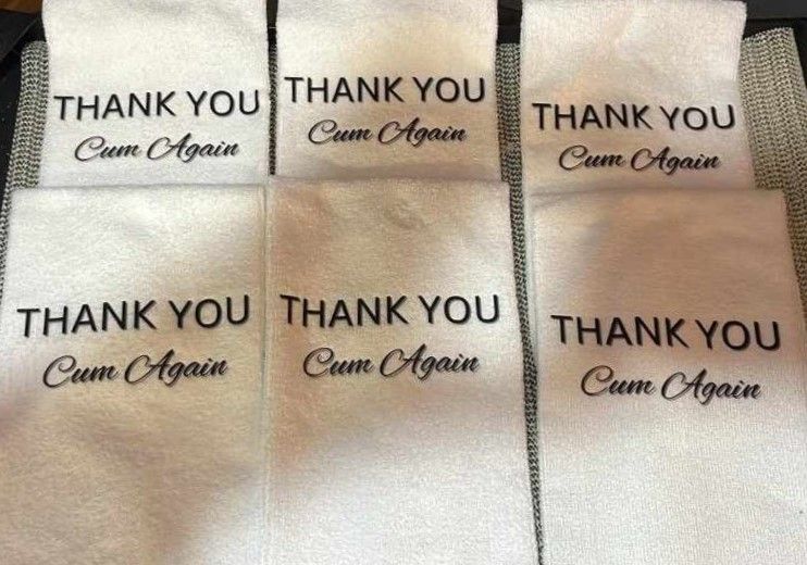 Stack of white promotional towels with custom embroidered text displayed on each towel.