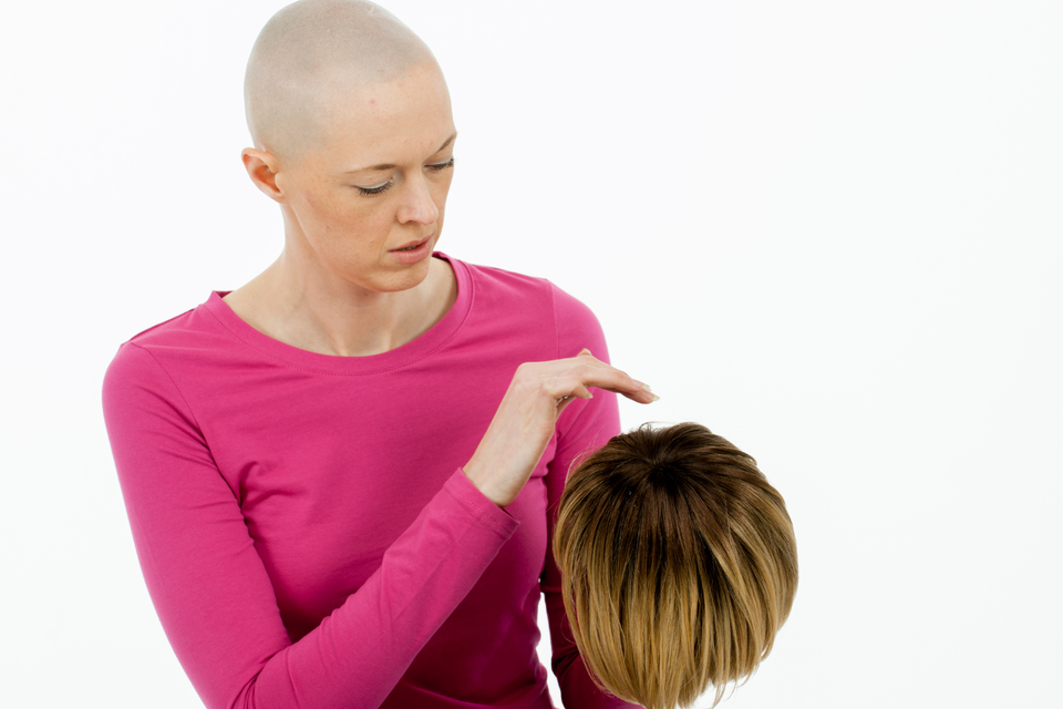 Person with hair loss holding a short wig while exploring hair replacement options for thinning hair and hair loss.