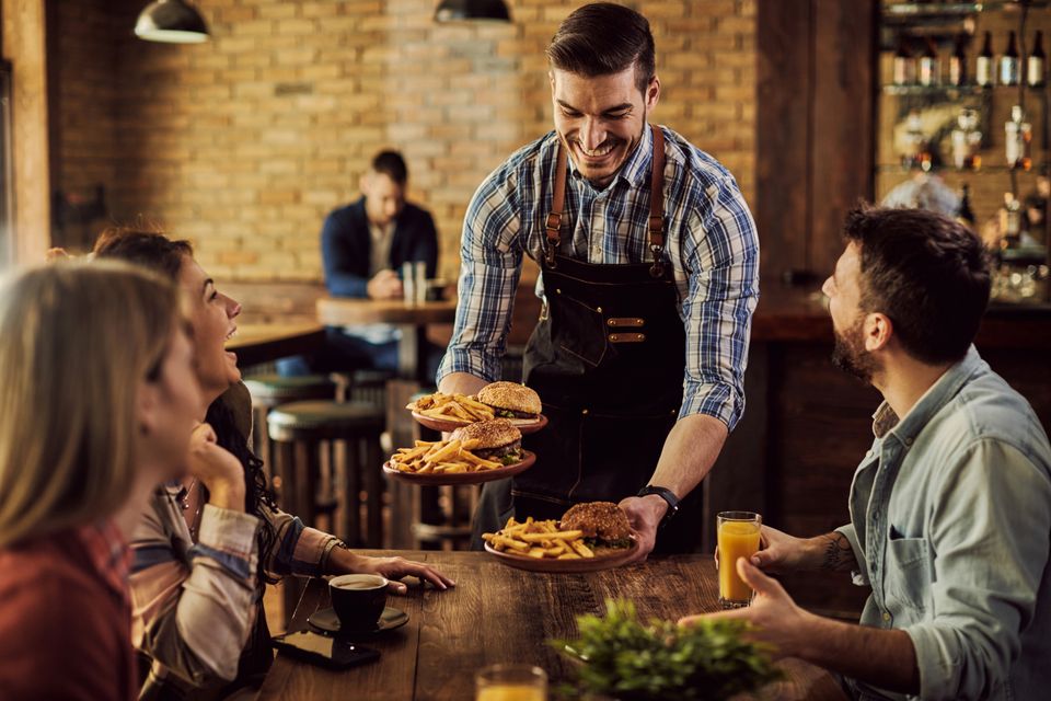 Happy waiter serving food group cheerful friends pub