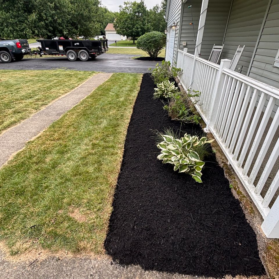 Front porch with fresh black mulch, hostas, ornamental shrubs, and landscaped garden beds surrounding the home's entrance