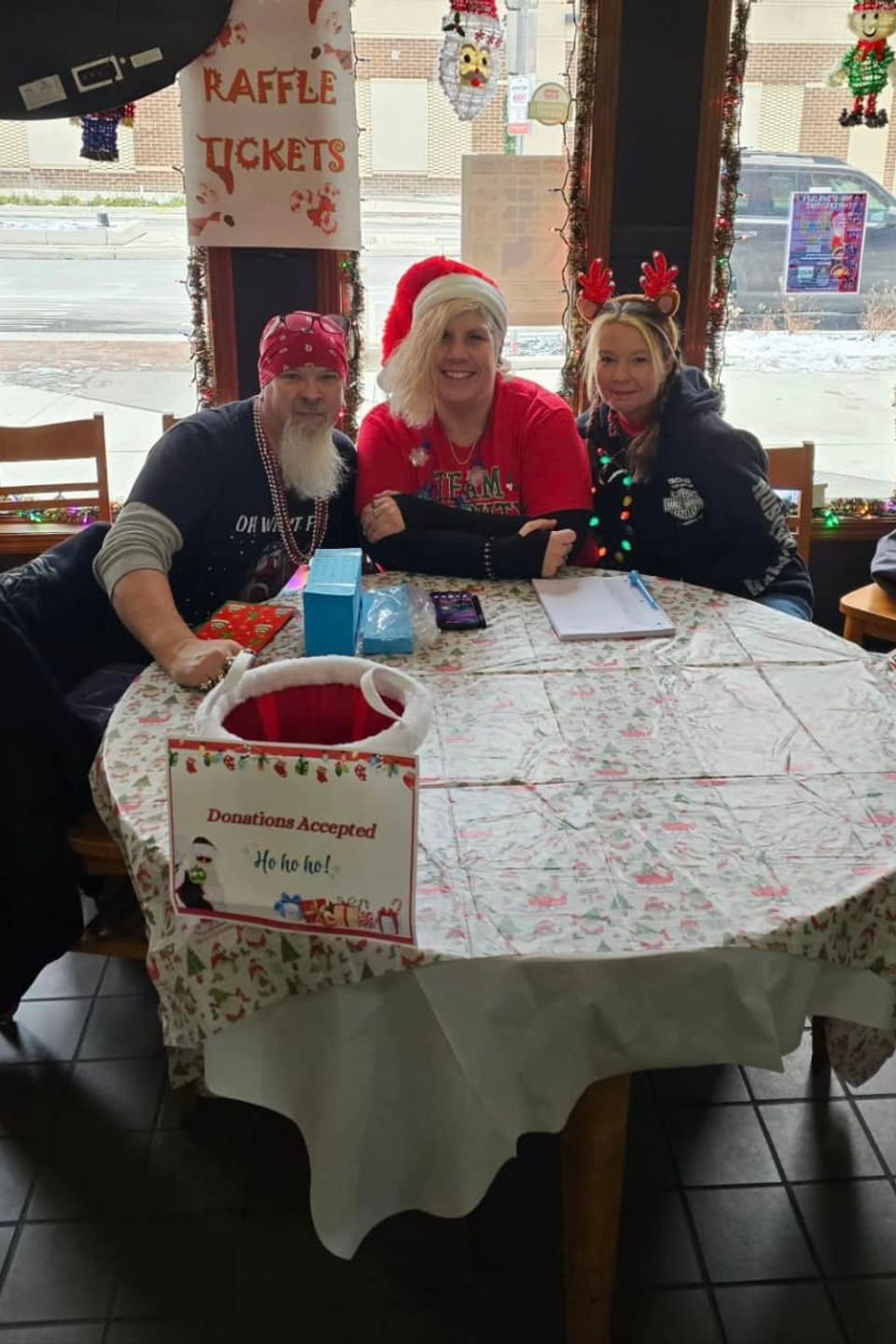 Three volunteers seated at a decorated table during a Christmas-themed fundraising event.