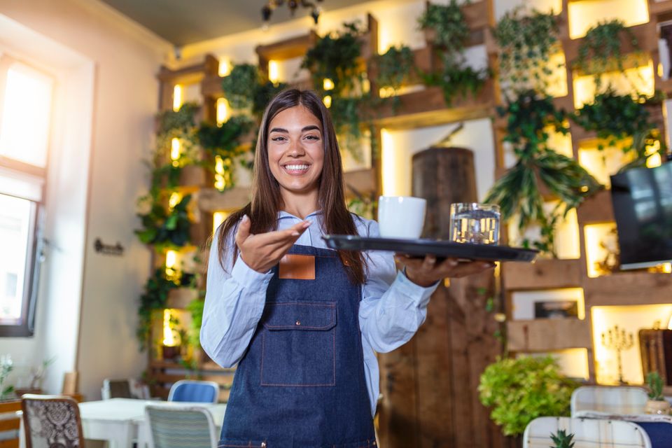 Happy waitress holding tray with cup coffee working cafeteria serves table