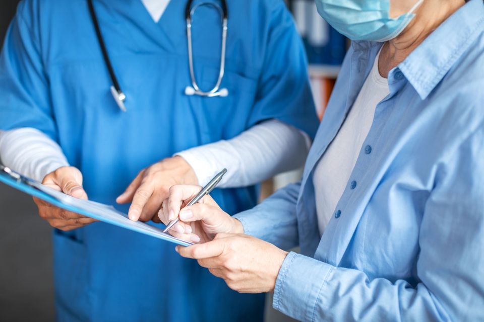 Smiling adult man doctor and elderly lady patient signing documents in clinic office