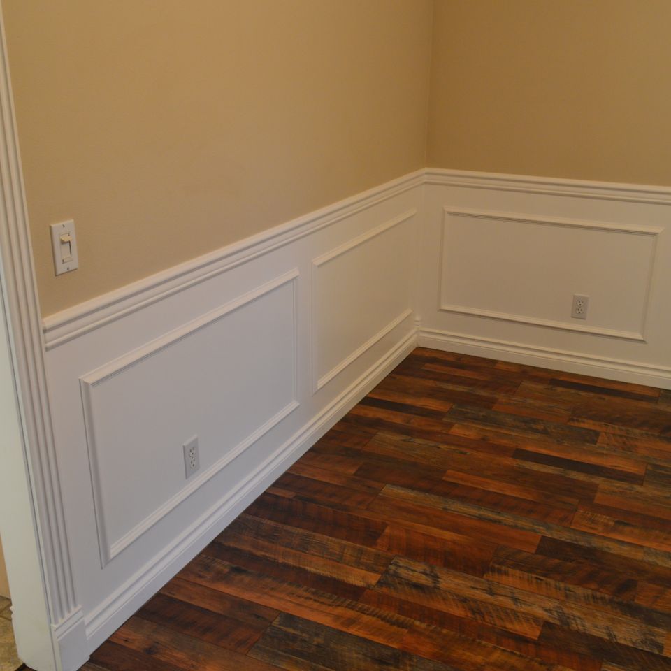 Raised panel wainscoting and white chair rail above reclaimed hardwood flooring in a custom home